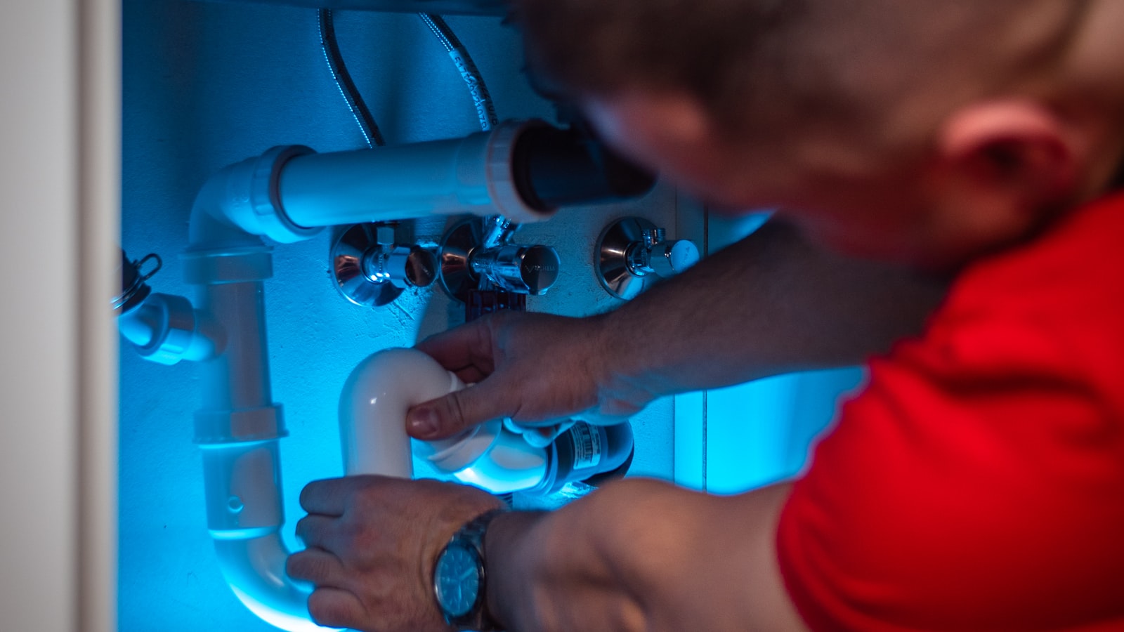 Hands setting a PVC P-trap under a sink.