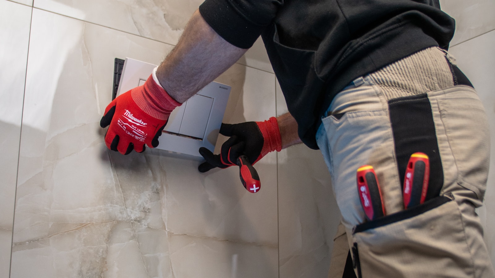 Installing a wall-hung flush plate on a tiled bathroom wall.