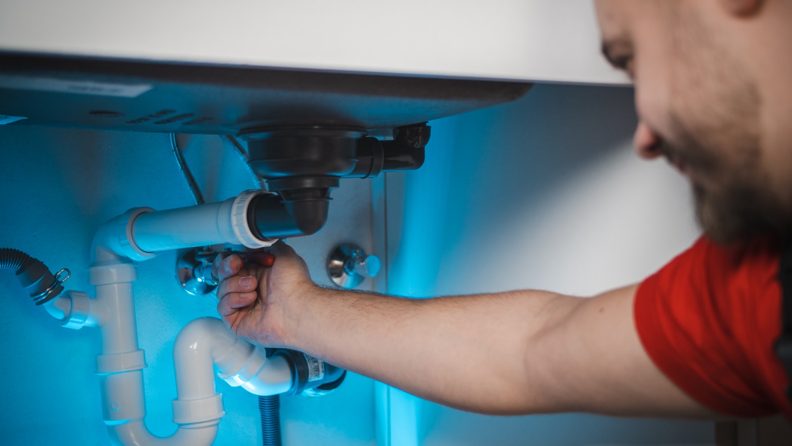 Plumber working shutoff valves and supply lines under a sink.